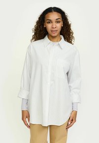 Cămașă cu nasturi și guler, albă cu dungi verticale albastre deschise, prevăzută cu buzunar la piept și manșete suflecate. Textură fină a materialului.