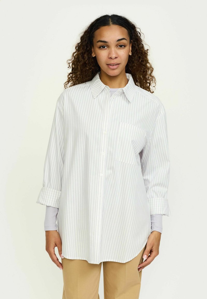 Cămașă cu nasturi și guler, albă cu dungi verticale albastre deschise, prevăzută cu buzunar la piept și manșete suflecate. Textură fină a materialului.