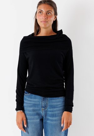Maglietta nera a maniche lunghe con scollatura a bardo e dettagli a coste. Abbinata a jeans in denim chiaro con vestibilità rilassata.