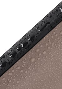 Materiale nero con una finitura lucida, che presenta gocce d'acqua, posato su una superficie beige opaca con una texture liscia e un leggero lucido.