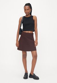 Svart cropped tank topp, brun vid skjørt og svarte klumpete loafers. Tilbehår inkluderer en svart veske med sølvdetaljer. Glatte teksturer.