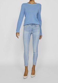 Blauer gestrickter Pullover mit langen Ärmeln, Rundhalsausschnitt, kombiniert mit hellblauen Skinny-Jeans und beigen High Heels.