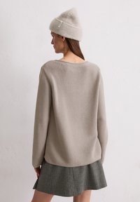 Lichtbeige gebreide trui met een losse pasvorm en een textuurpatroon, gecombineerd met een grijze rok. Wolachtige beanie in een vergelijkbare lichtbeige tint.