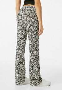 Pantalones acampanados con estampado floral en negro con margaritas blancas. Tela ligera con textura suave, con cintura alta y piernas acampanadas.