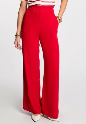 Red wide-leg trousers with a high elastic waistband, smooth texture, and side pockets; paired with beige pointed-toe heels.