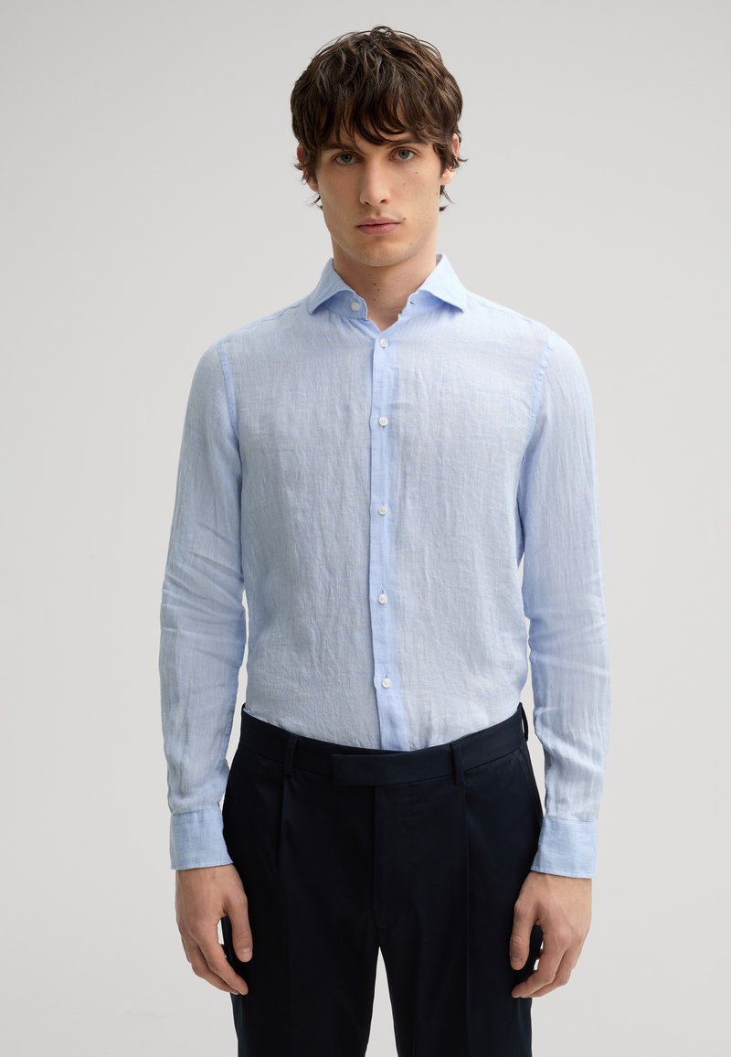 Camicia di lino azzurro chiaro con finitura testurizzata, dotata di una chiusura a bottoni e maniche lunghe, abbinata a pantaloni scuri.
