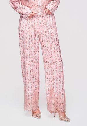 Szerokie spodnie w różowo-biały wzór z koronkową lamówką na nogawkach, zestawione ze srebrnymi sandałami na wysokim obcasie z paskami.