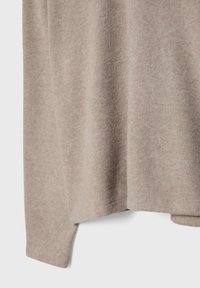 Beige gebreide trui met een zachte textuur, een losse pasvorm en zijsplitten aan de onderkant voor extra bewegingsvrijheid.