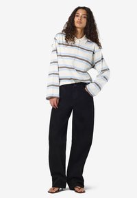 Μακρυμάνικο πουκάμισο πόλο ριγέ σε λευκό, ανοιχτό μπλε και καφέ, με κλασικό γιακά, συνδυασμένο με φαρδιά μαύρα παντελόνια με πλαϊνές τσέπες.