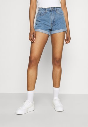 Pantalones cortos de mezclilla en azul claro, de tiro alto con dobladillos enrollados, combinados con zapatillas blancas y calcetines hasta el tobillo. Diseño simple y funcional.