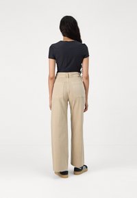 Helle beige weite Hosen mit zwei Gesäßtaschen, kombiniert mit einem schwarzen kurzärmeligen Oberteil. Das Material scheint weich mit einer glatten Textur zu sein.