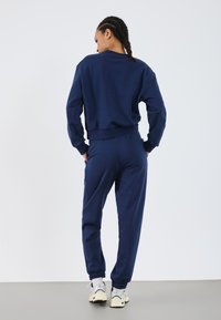 Navy blue sweatshirt and matching joggers made of soft fabric, featuring ribbed cuffs and waistband. Silver sneakers complete the outfit.