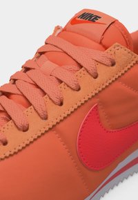 Tuvplāns ar oranžu Nike sporta apavu ar atbilstošām šņorēm, sarkanu swoosh logo un melnu Nike zīmolu uz mēles.