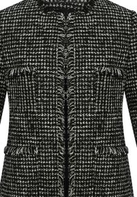 Černo-bílý tweedový saka s třepenými okraji, kulatým výstřihem a dvěma kapsami vpředu. Texturovaná tkanina s kostkovaným vzorem.