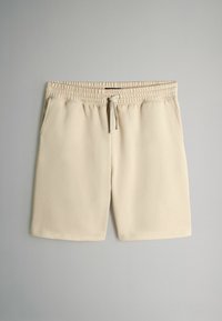 Beige shorts gemaakt van zachte stof met een elastische tailleband en verstelbaar trekkoord; beschikt over twee zijzakken.