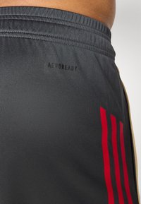 Shorts de sport noirs avec une texture lisse, arborant un logo "AEROREADY" noir et trois bandes verticales rouges sur le côté.