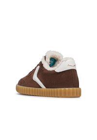Sneaker in suede marrone con accenti bianchi, fodera soffice e suola in gomma naturale. Presenta una punta arrotondata e un dettaglio di branding sottile.