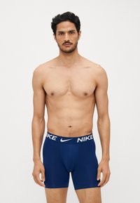 Navy blå Nike boxershorts med en kontrastfarvet hvid logo på taljebåndet. Glat stof, tætsiddende design og midt-lår længde.