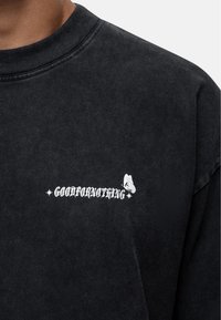 Black, textured sweatshirt with a round neck and white printed text "GOODFORNOTHING" and a butterfly accent, positioned on the front.