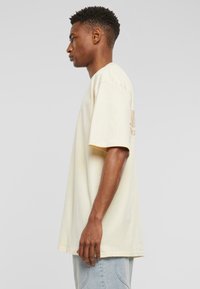Light yellow oversized t-shirt with short sleeves, featuring a subtle logo print on the back. Made of soft, smooth fabric.
