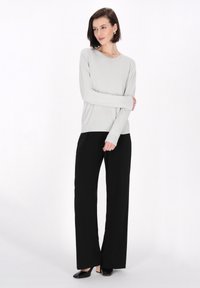 Hellgrauer Langarmpullover mit rundem Ausschnitt, kombiniert mit schwarzen weiten Hosen und schwarzen spitzen Schuhen, auf einem hellen Hintergrund.