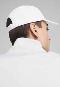 Gorra blanca con visera curvada y correa ajustable, combinada con una camisa blanca de cuello. Textura suave, diseño minimalista, esquema de color neutro.