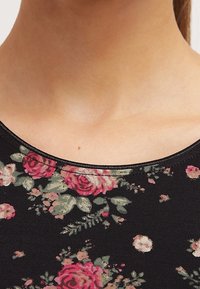 Tela negra con estampado floral que presenta rosas rosas y hojas verdes, escote redondo con una sutil textura acanalada, mangas cortas.