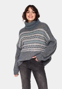 Pulover tricotat gros, cu un guler înalt, având modele albastre, gri și albe. Croi oversized, cu mansete și tiv râuri.
