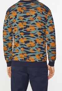 Stickad tröja med en marinblå bas och ett mönster av oranga palmer samt turkosa vågor. Ribbad mudd och nederkant, strukturerad tyg.