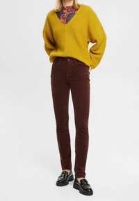 Mustard yellow knitted sweater with a V-neck and loose fit, paired with dark burgundy corduroy skinny pants. Black loafers complete the look.