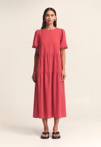 Abito maxi rosso a strati con maniche corte a sbuffo e scollatura arrotondata. Realizzato in tessuto leggero con una texture liscia.