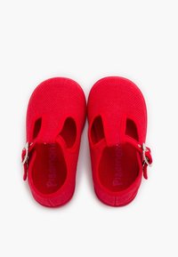 Zapatos de tela rojos con punteras redondeadas, una superficie texturizada, recortes laterales y un cierre de correa con hebilla plateada. Nombre de la marca visible en el interior.