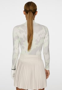 Langärmliges Oberteil in einem hellgrauen und grünen Ikat-Muster, kombiniert mit einem plissierten beigen Rock. Verfügt über ein tailliertes Design und weichen Stoff.