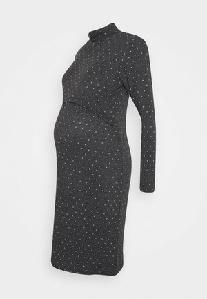 Robe de maternité gris foncé à manches longues avec des pois blancs et un col montant, conçue pour s’adapter à une silhouette enceinte.