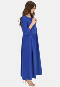 Długa, niebieska sukienka z gładkiego materiału, z okrągłym dekoltem, rękawami o długości trzech ćwiartek i rozkloszowanym dołem, który tworzy zwiewny kształt.