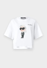 Baltas trumpas T marškinėliai, pagaminti iš medvilnės, su piešinėliu, vaizduojančiu asmenį akinių nuo saulės ir kostiumo, ant kurio yra "KARL LAGERFELD" užrašas.