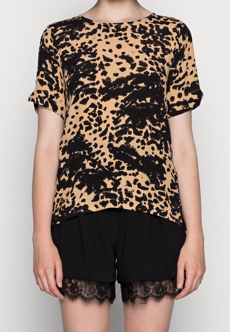 Haut à manches courtes avec imprimé léopard en beige et noir, présentant une coupe ample et un col rond, associé à un short noir avec une bordure en dentelle.