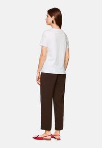 White cotton t-shirt, brown loose-fitting trousers, and red flat sandals with a bow detail, viewed from the back. Large round earrings.