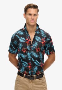 Camisa negra de manga corta con un patrón de hojas tropicales y flores rojas, confeccionada en una tela ligera, con cuello clásico y cierre de botones.