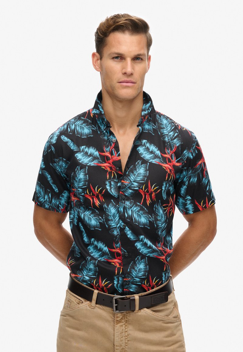 Camisa negra de manga corta con un patrón de hojas tropicales y flores rojas, confeccionada en una tela ligera, con cuello clásico y cierre de botones.