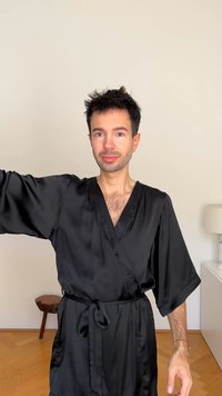 Sorte sateng kimono-kåpe med brede ermer, v-hals design og knyttet liv. Glatt tekstur med en lett glans. Enkel, elegant utførelse.