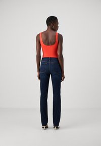 Κόκκινο αμάνικο τοπ και σκούρο μπλε τζιν. Το τοπ έχει σχήμα σκαφτού λαιμού και τα τζιν διαθέτουν κλασική γραμμή με πίσω τσέπες και λεπτομέρειες ραφής.