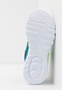 Biała gumowa podeszwa sportowego buta z teksturowanym gripem. Górna część w kolorze niebieskim i zielonym z czarnym akcentem. Design podkreśla funkcjonalność sportową.