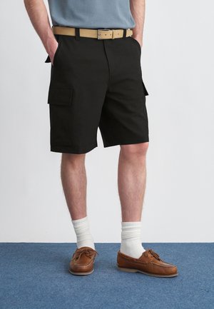 Pantaloncini cargo neri con tasche laterali, abbinati a una cintura beige, calzini bianchi a coste e scarpe da barca marroni. Design semplice e stile funzionale.
