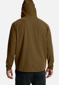 Brun huvtröja med en slät textur och raglanärmar. Har justerbar huva och en enkel, strömlinjeformad design.