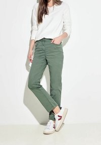 Pantalones cargo verdes de corte slim, con bolsillos delanteros y traseros, combinados con zapatillas blancas con detalles rojos y una camiseta blanca de manga larga.