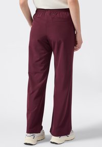 Bourgondische lichte broek met een elastische tailleband, rechte pijpen en een achterzak, gedragen met beige en marineblauwe sportschoenen.