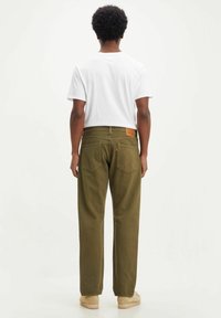 Pantalon en velours côtelé vert olive à coupe droite, avec poches arrière et une étiquette en cuir sur la ceinture. Associé à un t-shirt blanc.