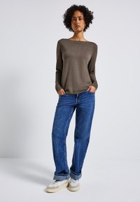 Brauner Langarm-Pullover mit Boot-Ausschnitt, kombiniert mit blauen hochgeschnittenen Jeans und weißen Sneakers mit grauen Akzenten. Glatte Textur.
