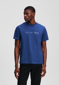 Mėlyna trumpa rankovė t-marškiniai iš medvilnės, su šiek tiek pakeltu logotipu "KARL LAGERFELD" per krūtinę, apvaliu kaklu ir laisvu siluetu.